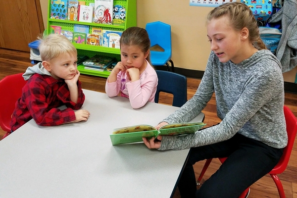 Middle school student reading to preschool students.