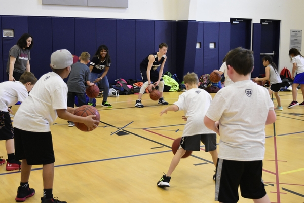 High school students showing elementary students how to dribble a basketball.